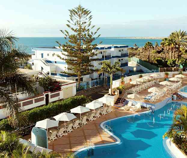 Bilde av et hotellområde med basseng, solsenger og utsikt over havet. (AI-generert tekst)