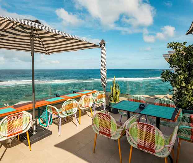 Uteservering med fargerike stoler og utsikt over havet. (AI-generert tekst)