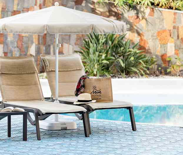 To solsenger med parasoll ved et basseng, med en Juicy motellveske og en hatt. (AI-generert tekst)