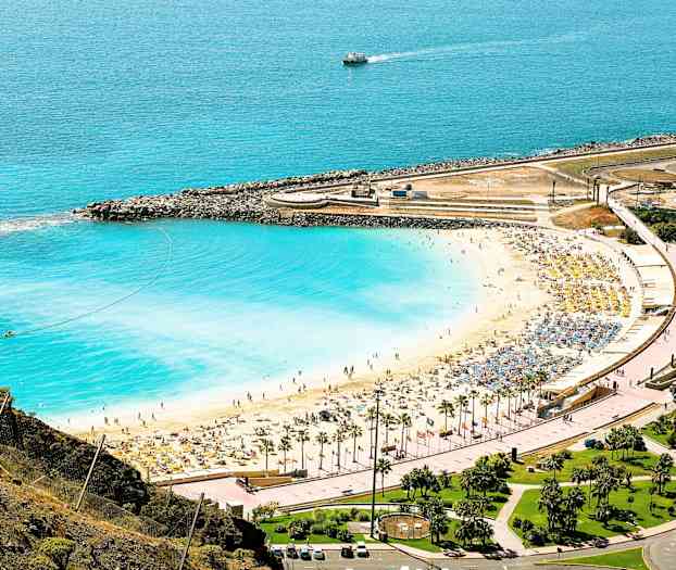 En strand med hvit sand og blått vann ved en kystlinje med solsenger og parasoller. (AI-generert tekst)