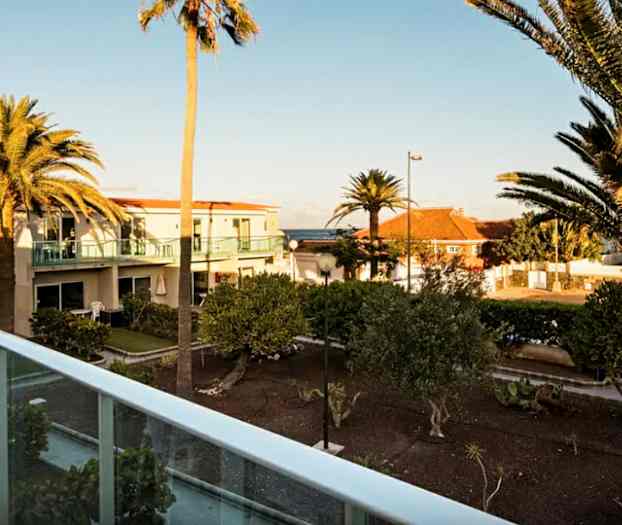 Utendørs utsikt med palmer og bolighus i bakgrunnen, tatt fra en balkong. (AI-generert tekst)