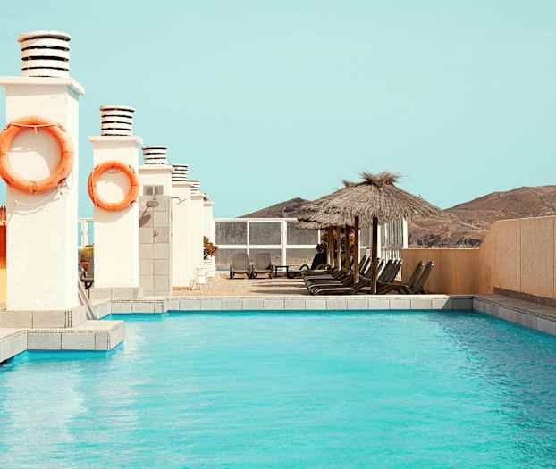 Utendørsbasseng med solsenger og parasoller ved siden. (AI-generert tekst)