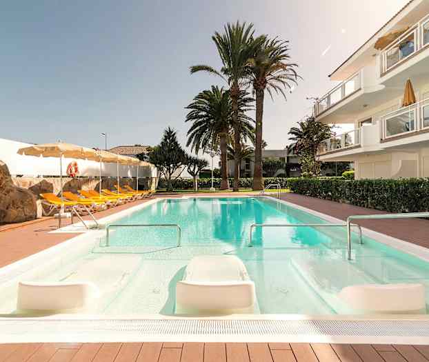 Bassengområde med solsenger, parasoller, en steinmur og omkringliggende trær. (AI-generert tekst)