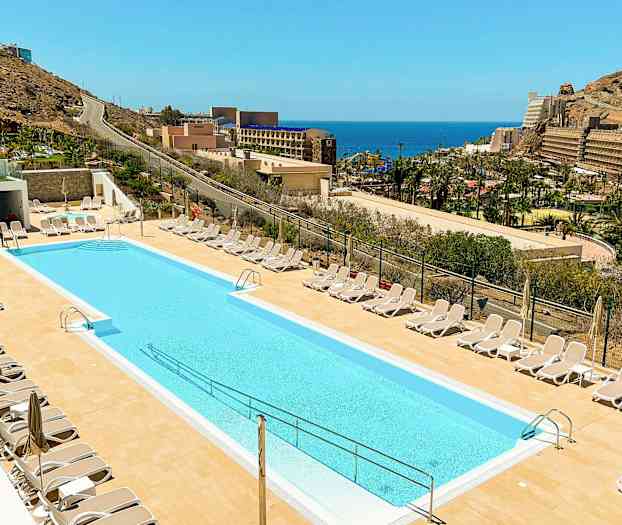 Et utendørs svømmebasseng omgitt av solsenger med havutsikt i bakgrunnen. (AI-generert tekst)