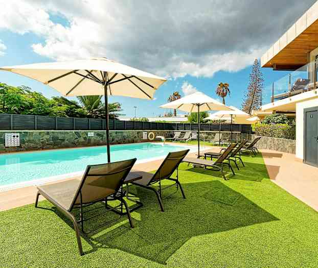 Et utendørsbasseng med solsenger og parasoller på gress og terrasse. (AI-generert tekst)