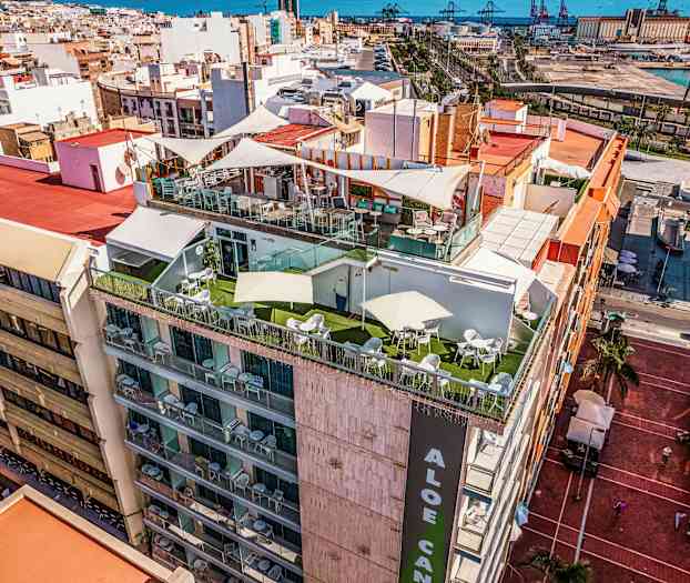 En bygning med terrasser på toppen, omgitt av en by med havet i bakgrunnen. (AI-generert tekst)