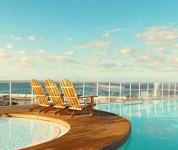 Tre trestoler ved kanten av et basseng med utsikt over havet. (AI-generert tekst)