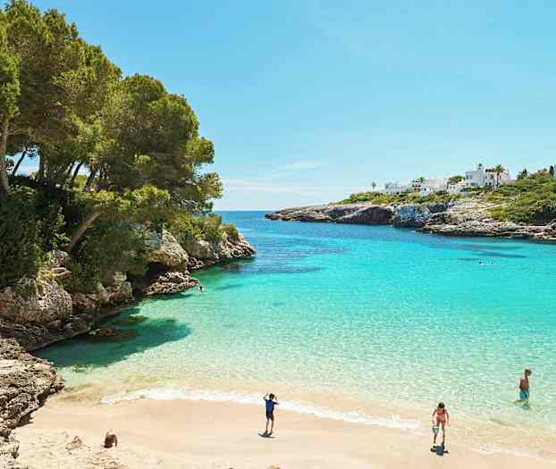 En vik med turkist vann, sandstrand og omkringliggende klipper. (AI-generert tekst)