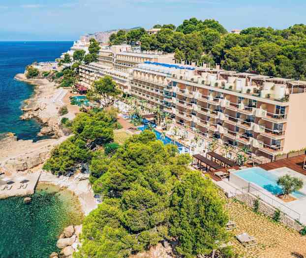 Fleretasjes hotell ved kysten med et svømmebasseng foran og omgivende vegetasjon. (AI-generert tekst)