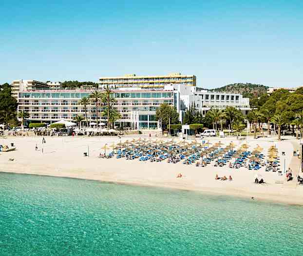 En strand med parasoller og solsenger foran en stor bygning med balkonger. (AI-generert tekst)