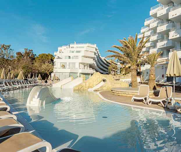 Bassengområde med solsenger og parasoller ved hotellbygning. (AI-generert tekst)