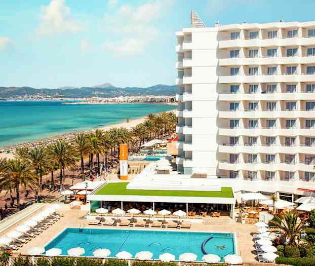 Hotell ved stranden med basseng og solsenger, hav i bakgrunnen. (AI-generert tekst)