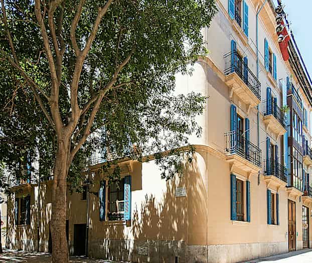 En bygning med flere balkonger og blå vinduslemmer. (AI-generert tekst)