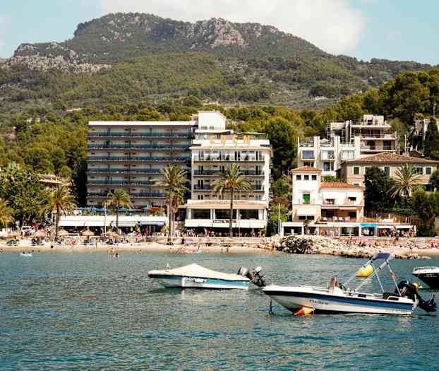 Et bilde av en kystby med hotell, strand og båter ved vannet. (AI-generert tekst)