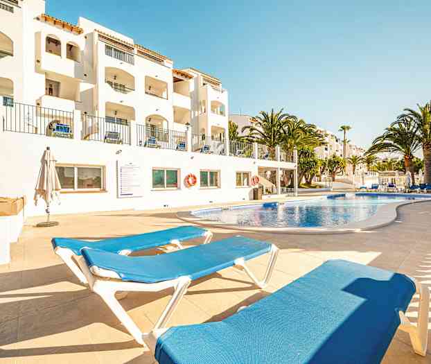 Utendørs svømmebasseng med solsenger og hvite bygninger i bakgrunnen. (AI-generert tekst)