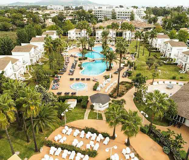 Et feriehotell med bassengområde, grøntarealer og bygninger i bakgrunnen. (AI-generert tekst)