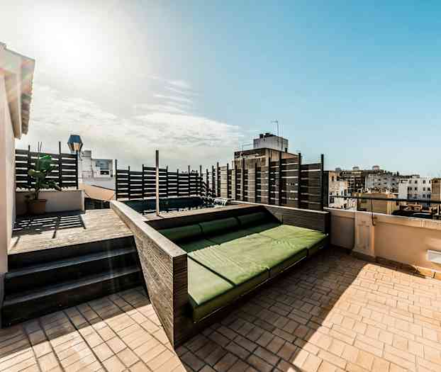 En takterrasse med en grønn sitteplass og utsikt over omkringliggende bygninger. (AI-generert tekst)