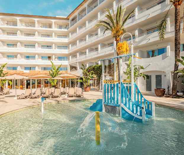 Utendørs bassengområde med lekeplass for barn og solsenger foran hotellbygning. (AI-generert tekst)