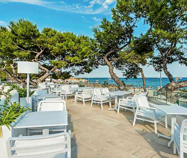 Uteservering med hvite møbler og utsikt over havet og stranden. (AI-generert tekst)