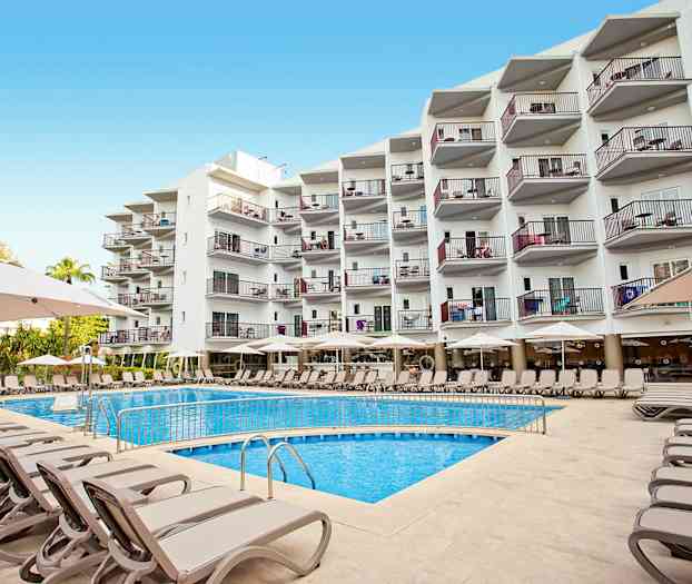 Flere solsenger og parasoller ved et utendørs svømmebasseng foran en bygning med flere etasjer. (AI-generert tekst)