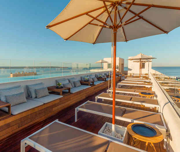 Utsikt over en moderne takterrasse med solsenger og parasoller mot havet. (AI-generert tekst)