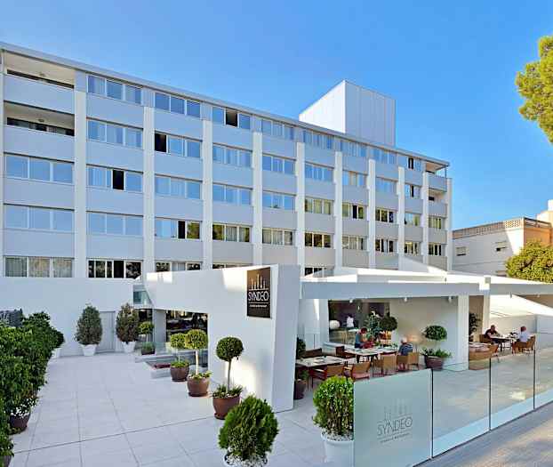 Bilde av en moderne hotellbygning med flere etasjer, utendørs servering og planter utenfor. (AI-generert tekst)