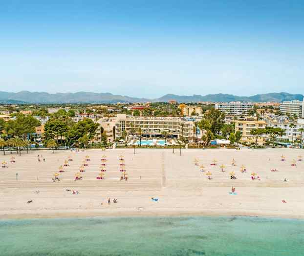 Strand med solsenger og parasoller, hotell og bysilhuett i bakgrunnen. (AI-generert tekst)