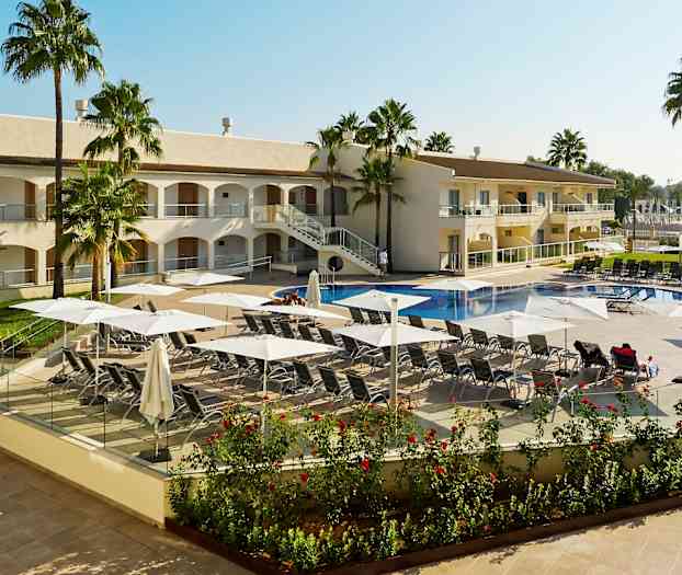 Bilde av et hotellbasseng med solsenger og parasoller, omgitt av palmer og hotellet. (AI-generert tekst)