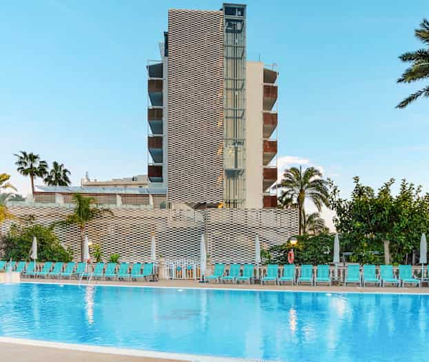 En bygning med et basseng foran samt palmer og solsenger. (AI-generert tekst)