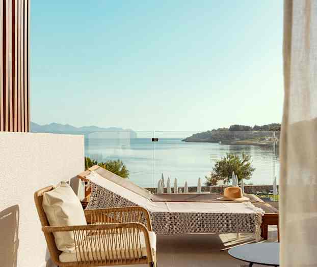 Utsikt fra en terrasse med en solseng og glassrekkverk, sjøen og landskapet vises i bakgrunnen. (AI-generert tekst)