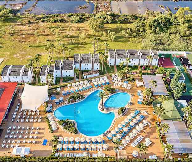 Utsikt fra luften over et hotellområde med bassenger, solsenger og hvitmalte bygninger omgitt av grøntområder. (AI-generert tekst)