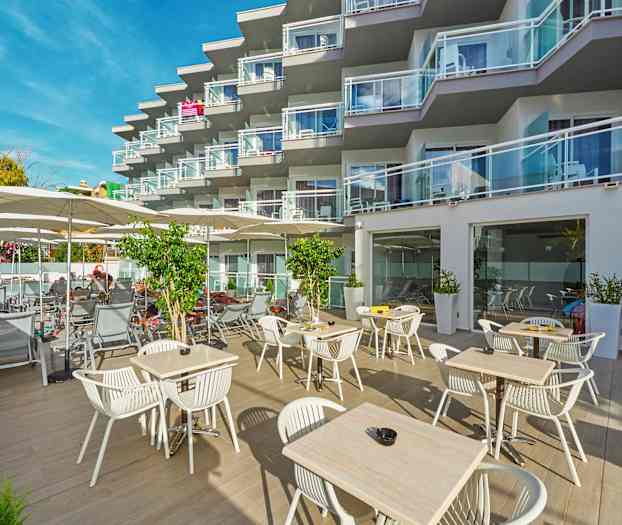 Utendørsområde med bord og stoler samt solsenger ved et hotell med balkonger. (AI-generert tekst)