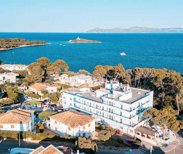 Luftfoto av et kystområde med bygninger, hus nær stranden og havutsikt med en liten øy i bakgrunnen. (AI-generert tekst)