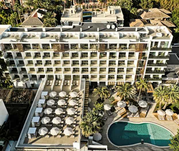 Luftfoto av et hotell med et basseng og en stor terrasse med parasoller og solsenger. (AI-generert tekst)