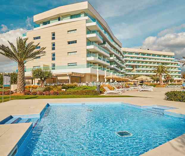 Bilde av et hotell med moderne bygninger, et svømmebasseng og utendørs loungeområder. (AI-generert tekst)