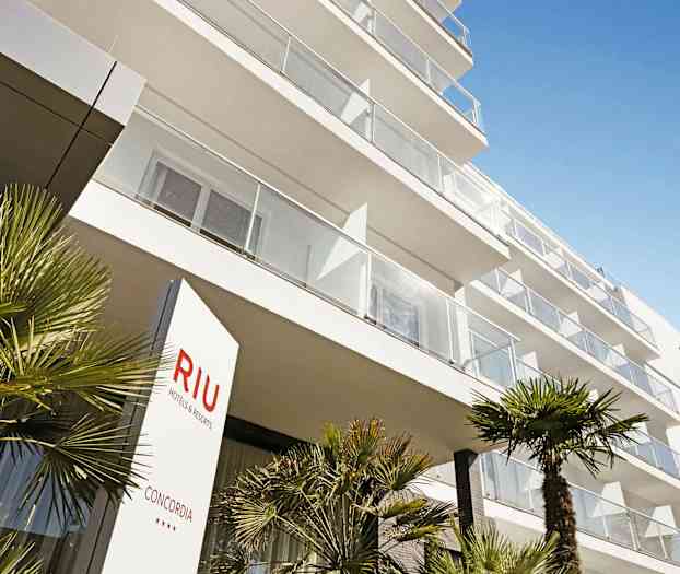 En moderne hotellbygning med balkonger og palmer i forgrunnen. (AI-generert tekst)