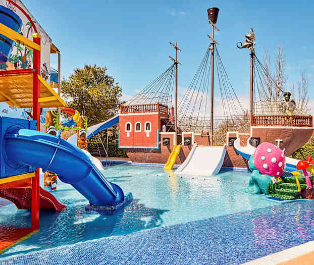 Bilde av en vannpark med et pirattematisk skip, fargerike sklier og lekeskulpturer i et basseng. (AI-generert tekst)