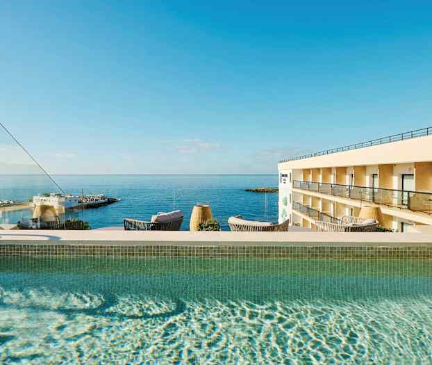 Utendørs svømmebasseng med utsikt mot havet og en hotellbygning. (AI-generert tekst)