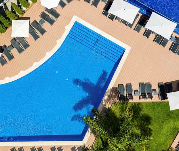 Luftfoto av et basseng omgitt av solsenger og parasoller. (AI-generert tekst)