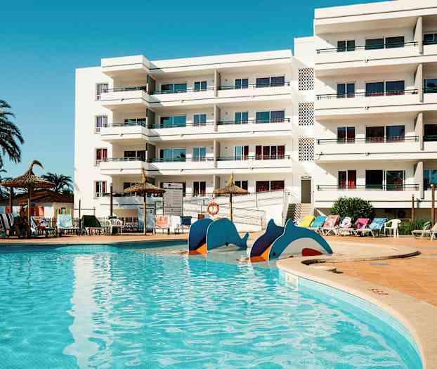 Et svømmebasseng foran en hvit bygning med balkonger. (AI-generert tekst)