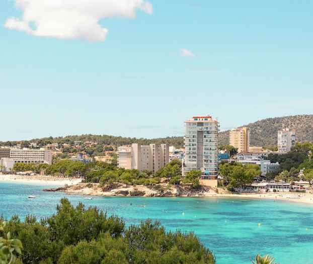 En kystby med hotellbygninger ved en strand og klart turkis vann. (AI-generert tekst)