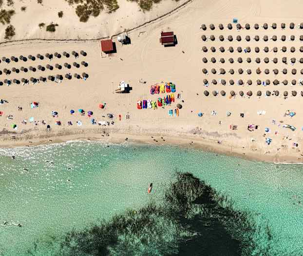 Luftfoto av en strand med parasoller, mennesker og klart vann. (AI-generert tekst)