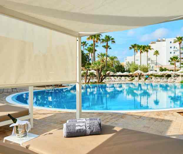 En luksuriøs cabana nær et basseng med palmer og parasoller rundt omkring. (AI-generert tekst)