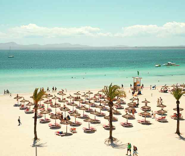 Strand med parasoller, solsenger og personer; havet i bakgrunnen. (AI-generert tekst)