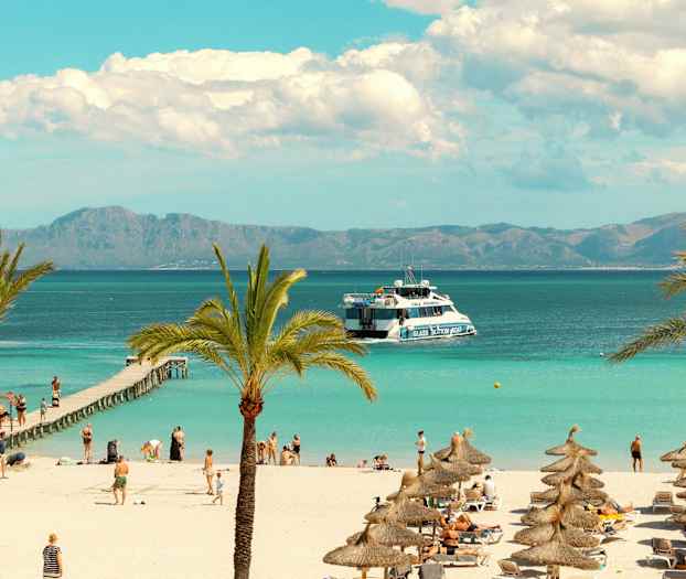 Strand med palmer og parasoller samt turister ved en brygge og en båt på havet. (AI-generert tekst)