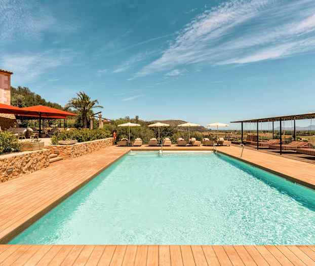 Et utendørsbasseng med solsenger og parasoller rundt, omgitt av natur og landskap. (AI-generert tekst)