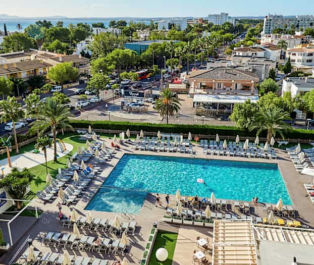 Et basseng omgitt av solsenger, med omkringliggende grøntområder og bygninger i bakgrunnen. (AI-generert tekst)