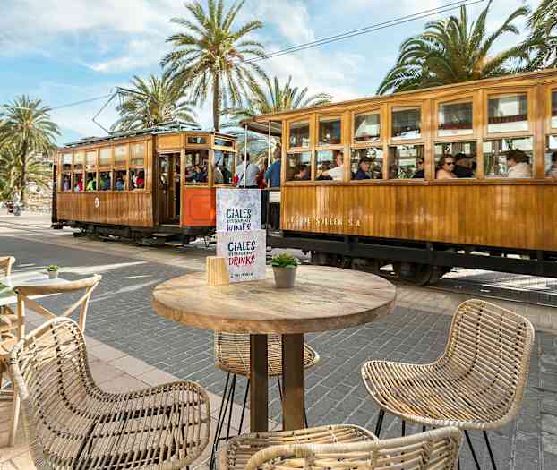 En tresporvogn passerer ved et torg med bord og stoler. (AI-generert tekst)