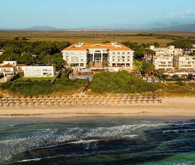 Utsikt over en strand med solsenger og parasoller foran et hotell omgitt av vegetasjon. (AI-generert tekst)