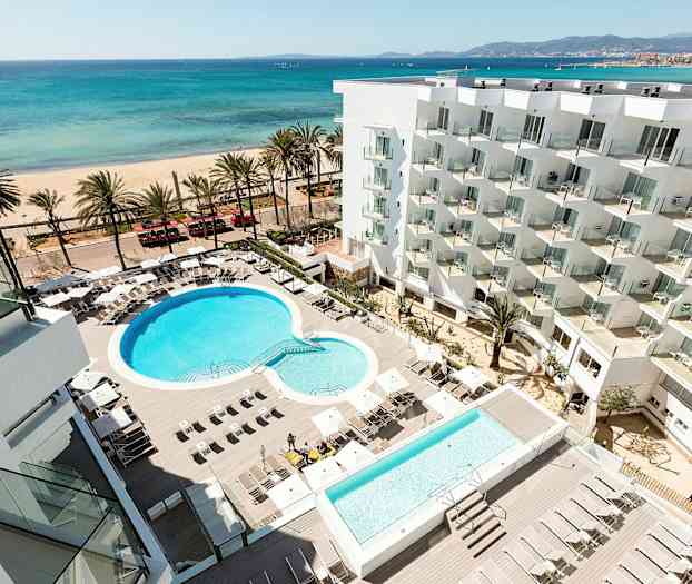 Hotellområde med basseng og solsenger, strand og hav i bakgrunnen. (AI-generert tekst)